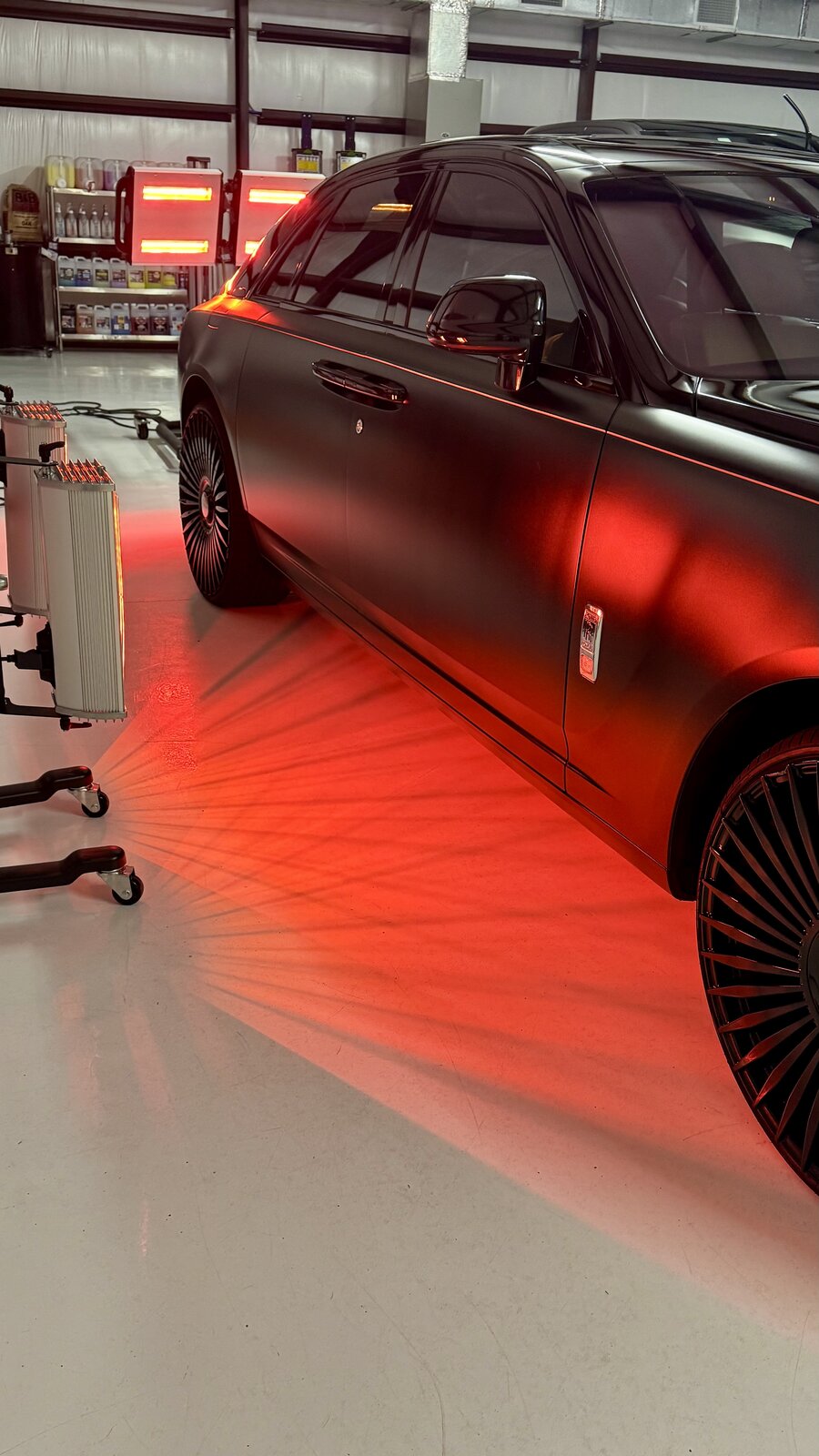 Matte black Rolls-Royce under infrared curing lamps in the studio